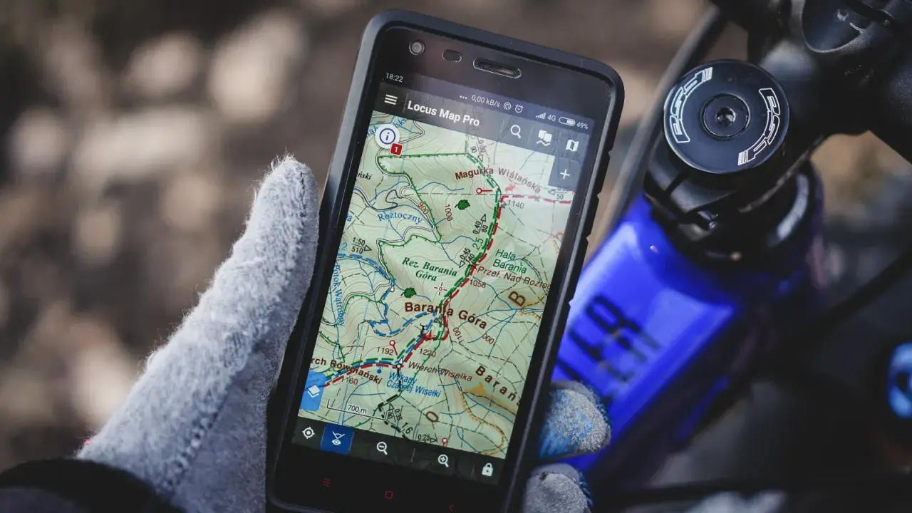 Rękawiczka trzyma smartfon z mapą górską, pokazującą darmowa aplikacja na rower. Idealna do nawigacji w terenie.