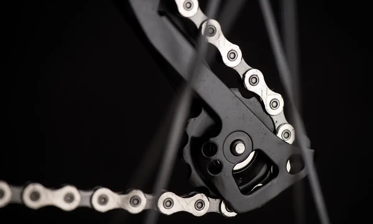 Zbliżenie na mechanizm przerzutki z łańcuchem rowerowym. Widać ogniwa i rolki, kluczowe dla łańcuch rowerowy wymiary.