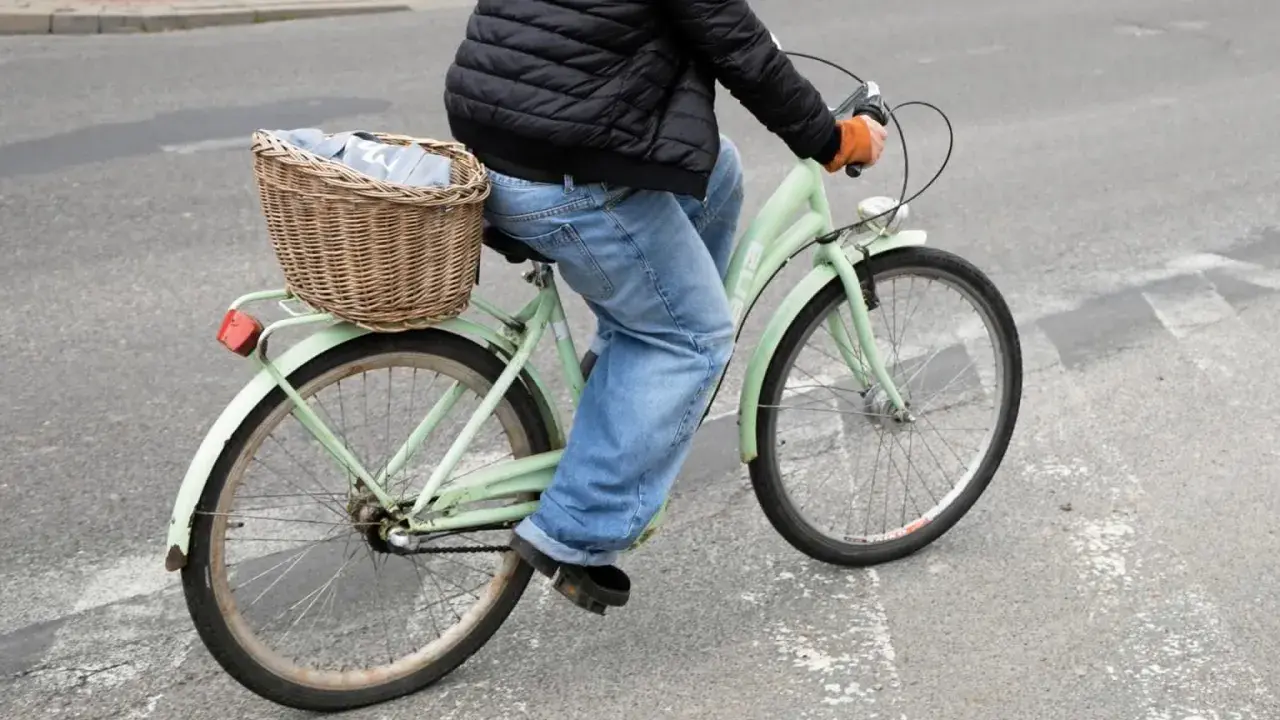 Osoba na rowerze z koszykiem pełnym ubrań wykonuje przejazd rowerem przez pasy.
