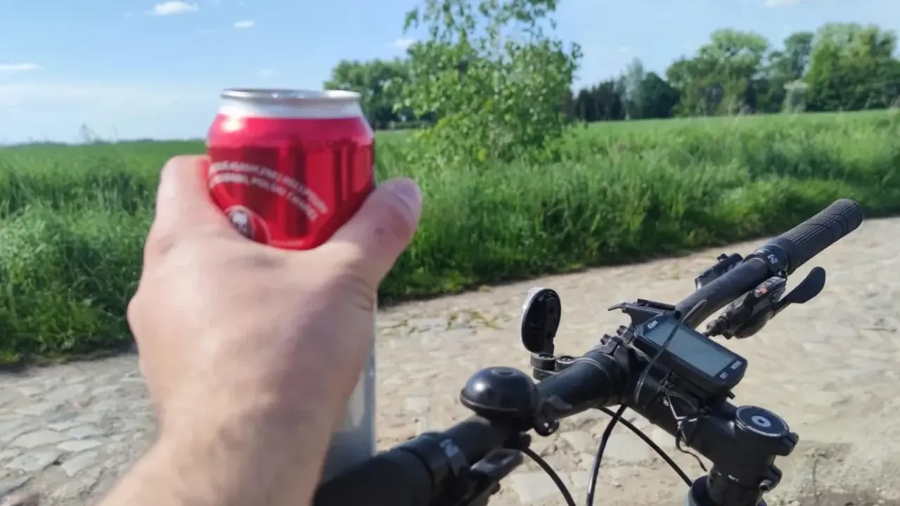 Rowerzysta trzyma puszkę napoju, co sugeruje kierowanie rowerem w stanie nietrzeźwości. Na kierownicy widoczny licznik.