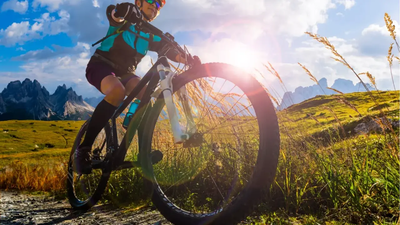 Kobieta na rowerze MTB w górach, słońce przebija się przez chmury. To wolność i przygoda!