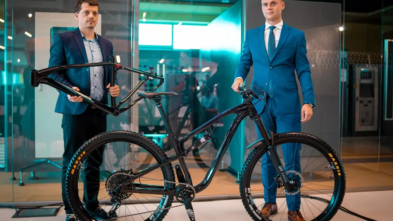 Dwóch mężczyzn prezentuje nowy rower full-suspension. Jeden trzyma ramę, drugi stoi przy gotowym rowerze. To duma firmy Romet.