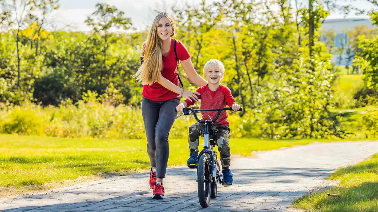 Mama pomaga synkowi w nauce jazdy na rowerze w słoneczny dzień w parku.