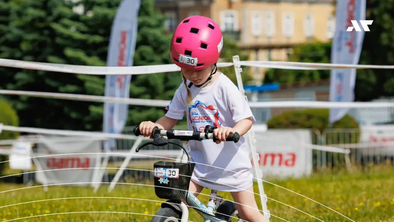 Dziewczynka w różowym kasku na rowerze, z numerem 30. Czy kask na rower dla dziecka jest obowiązkowy? Tak, dla bezpieczeństwa!