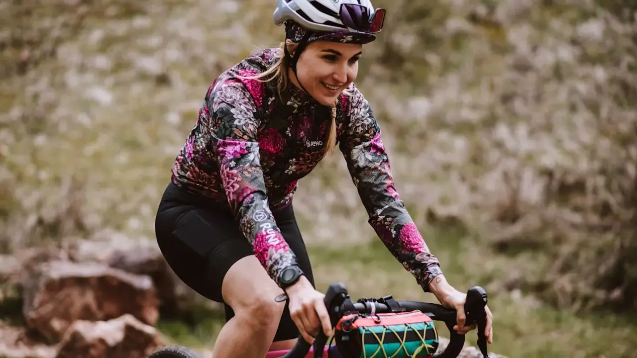 Uśmiechnięta rowerzystka w kwiecistej bluzie pokonuje kolejne kilometry. Dziś cel to 50 km na rowerze po górskich ścieżkach.