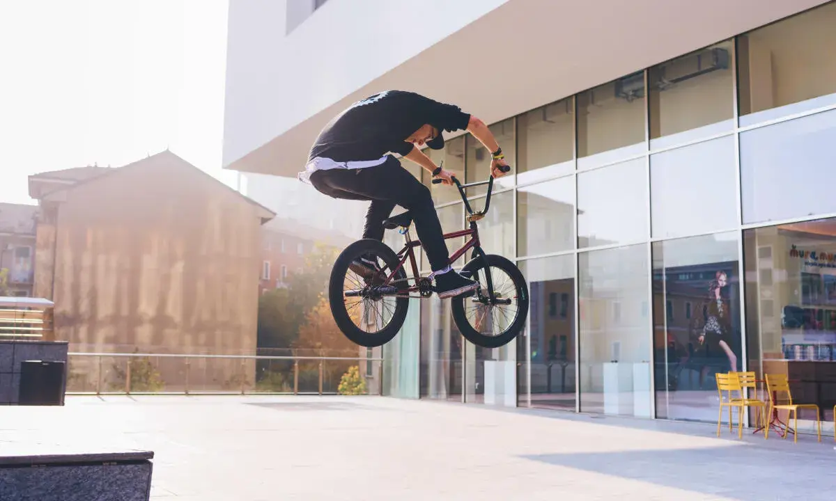 Chłopak na BMX-ie wykonuje bunny hop, unosząc rower w powietrze przed nowoczesnym budynkiem.