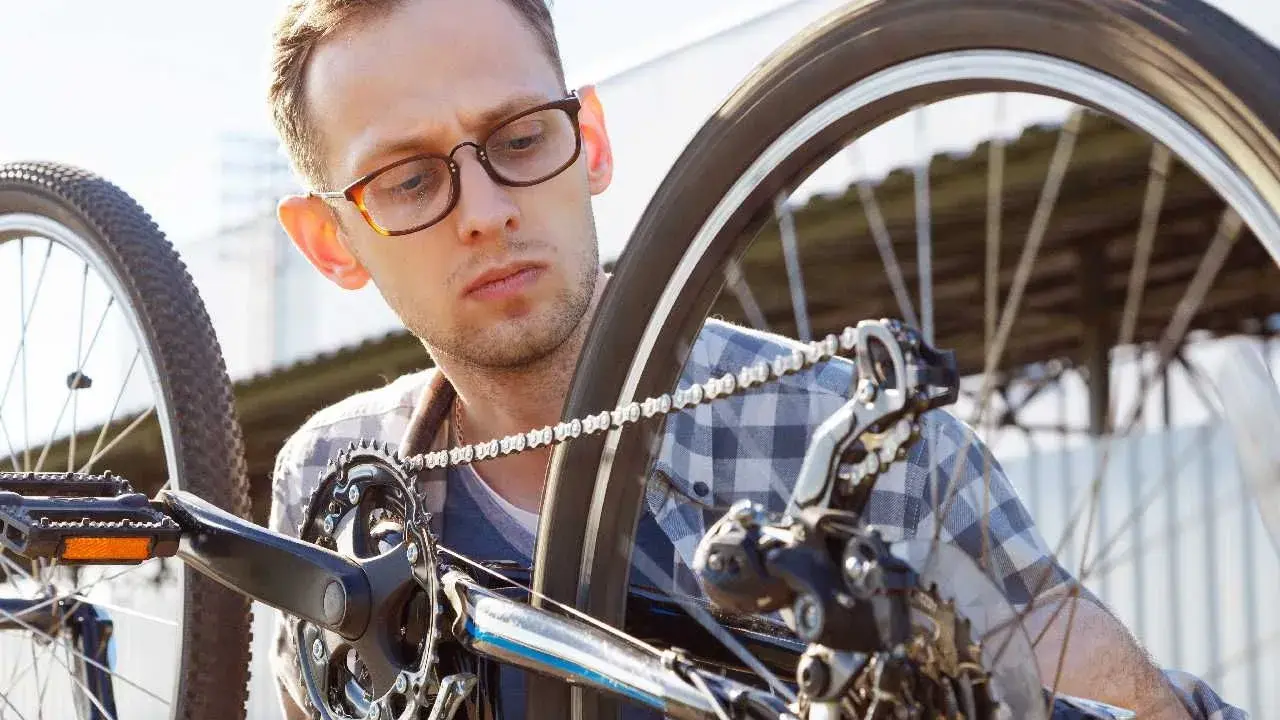 Mężczyzna w okularach sprawdza rozmiary kół rowerowych, skupiony na mechanizmie przerzutek i łańcuchu.