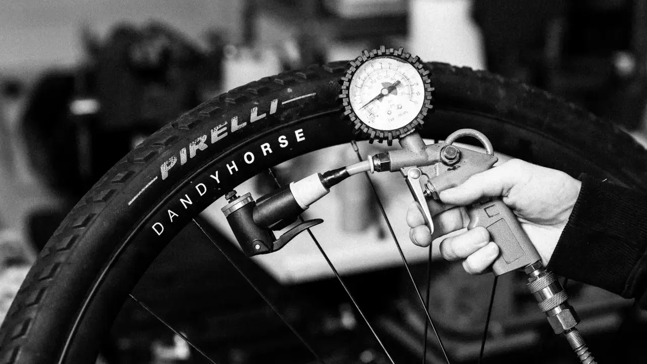 Ręka trzyma pompkę z manometrem, pompując oponę rowerową Pirelli Dandy Horse. Brak dętki.