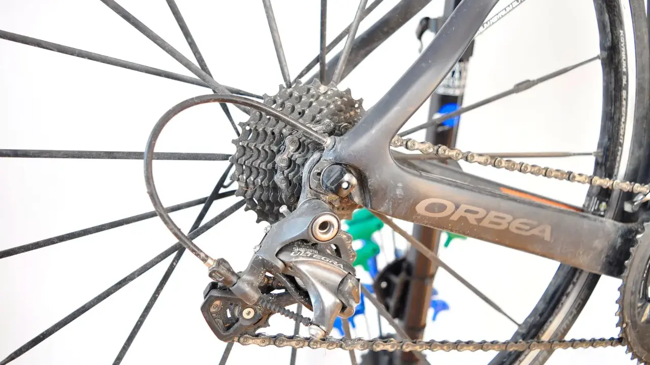 Tylna przerzutka Shimano Ultegra, kluczowy element przekładni rowerowej, na tle koła i ramy Orbea.