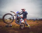 Młody motocyklista ćwiczy jazdę na jednym kole na błotnistym polu.