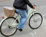 Osoba na rowerze z koszykiem pełnym ubrań wykonuje przejazd rowerem przez pasy.