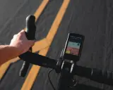 Rowerzysta trzyma kierownicę, na której zamontowana jest aplikacja na rower iPhone z mapą i danymi o trasie.
