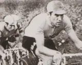 Dwóch kolarzy w akcji. Na pierwszym planie widać zawodnika w czarnych spodenkach i jasnej koszulce, zdeterminowanego jak zawsze Eddy Merckx.