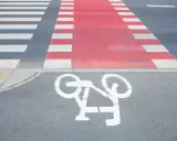 Czerwone pasy dla rowerzystów przecinają przejście dla pieszych. Symbol roweru na asfalcie zaprasza do bezpiecznej jazdy.
