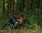 Para jadąca na rowerach górskich przez las. Czy to gravel, czy MTB? Trudno powiedzieć, ale zabawa jest przednia!