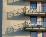 Dwa rowery stoją na balkonach, tworząc ciekawe cienie na ścianie budynku. Praktyczne przechowywanie roweru na balkonie.