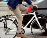 Elegancki rowerzysta na chodniku, obok czarnego samochodu i białego skutera.