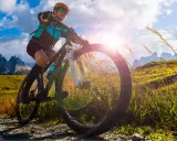 Kobieta na rowerze MTB w górach, słońce przebija się przez chmury. To wolność i przygoda!