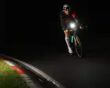 Kolarz w kasku z czaszką jedzie nocą, oświetlając drogę mocnym światłem. Czy rower musi mieć włączone światła w dzień? To pytanie nabiera sensu, gdy widzimy taką jazdę.
