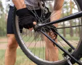 Rowerzysta w rękawiczkach reguluje **scentrowane koło** w lesie.