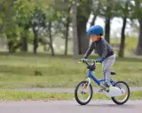 Chłopiec w kasku na rowerze 12 cali, idealnym na jego wzrost, uczy się jeździć po parku.