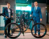Dwóch mężczyzn prezentuje nowy rower full-suspension. Jeden trzyma ramę, drugi stoi przy gotowym rowerze. To duma firmy Romet.