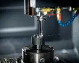Precyzyjna obróbka metalu na maszynie CNC. Wiertło precyzyjnie pracuje nad elementem, a chłodziwo rozpryskuje się wokół. Sztywne osie maszyny gwarantują dokładność.