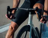 Kolarz w czarnych spodenkach i białych skarpetkach trzyma kierownicę aerodynamicznego roweru Orbea. Szytka rowerowa jest gotowa do jazdy.