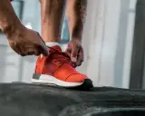 Mężczyzna wiąże czerwone buty sportowe, idealne jako buty na siłownię. Gotowy do treningu.