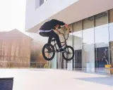 Chłopak na BMX-ie wykonuje bunny hop, unosząc rower w powietrze przed nowoczesnym budynkiem.