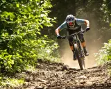 Kolarz MTB w pełnym skupieniu, z zachowaniem prawidłowej pozycji na rowerze, zjeżdża po kamienistym szlaku, wzbijając tumany kurzu.