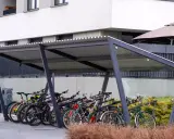 Rzędy rowerów czekają na swoich właścicieli pod nowoczesną wiatą. Bezpieczne przechowywanie roweru na dworze to wygoda i ochrona przed deszczem.