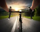 Rowerzysta w rękawiczkach mija pola i lasy, celując w zachód słońca. Dziś na liczniku pojawi się 100 km na rowerze.