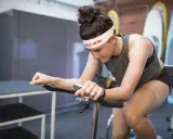 Kobieta w opasce Red Bull wykonuje intensywne interwały na rowerze stacjonarnym, skupiona na treningu.