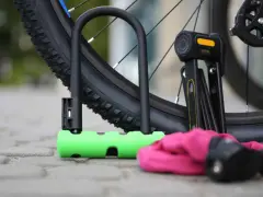 Solidne zabezpieczenie roweru przed kradzieżą: zielona U-lock i składany czarny zapięcie leżą obok opony.