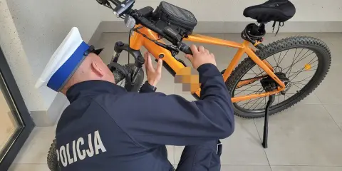 Policjant sprawdza, czy na rower elektryczny trzeba mieć prawo jazdy. Pomarańczowy rower z sakwą na kierownicy.