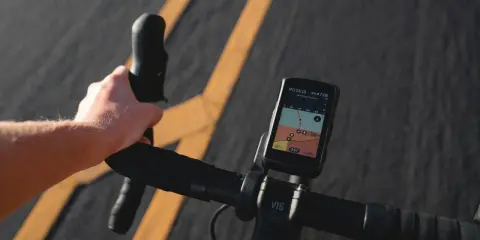 Rowerzysta trzyma kierownicę, na której zamontowana jest aplikacja na rower iPhone z mapą i danymi o trasie.