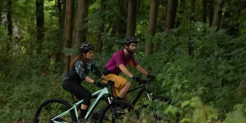 Para jadąca na rowerach górskich przez las. Czy to gravel, czy MTB? Trudno powiedzieć, ale zabawa jest przednia!