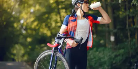 Kolarz w kasku i stroju sportowym pije wodę z bidonu. To ważny element diety kolarza, by uzupełnić płyny po wysiłku.