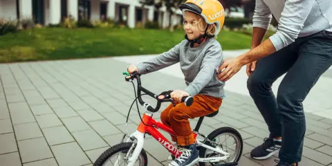 Chłopiec w kasku na rowerku 16 cali, idealnym na wiek 4-6 lat, uczy się jeździć z pomocą taty.