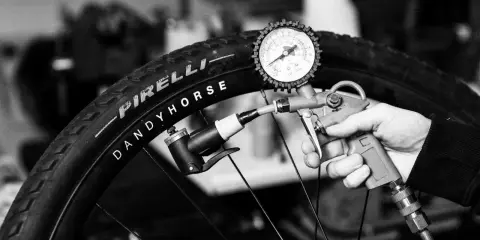 Ręka trzyma pompkę z manometrem, pompując oponę rowerową Pirelli Dandy Horse. Brak dętki.