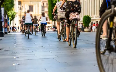 Grupa osób jedzie rowerem po chodniku w słoneczny dzień.