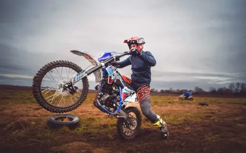 Młody motocyklista ćwiczy jazdę na jednym kole na błotnistym polu.