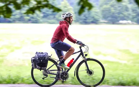 Mężczyzna w kasku jedzie na rowerze trekkingowym z sakwami. Idealny na wycieczki!