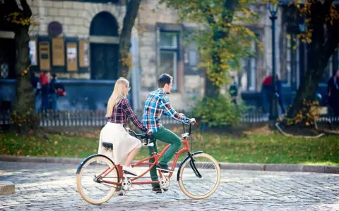 Para co to? Para na rowerze typu tandem przemierza brukowaną uliczkę w jesiennym mieście.
