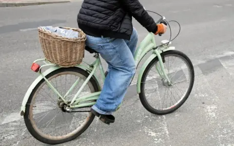 Osoba na rowerze z koszykiem pełnym ubrań wykonuje przejazd rowerem przez pasy.
