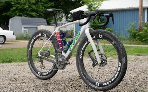 Biały rower gravelowy z szerokimi oponami i sakiewką na kierownicy, gotowy na przygodę. Czy to gravel czy szosa, zależy od terenu!