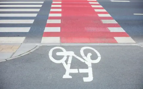 Czerwone pasy dla rowerzystów przecinają przejście dla pieszych. Symbol roweru na asfalcie zaprasza do bezpiecznej jazdy.