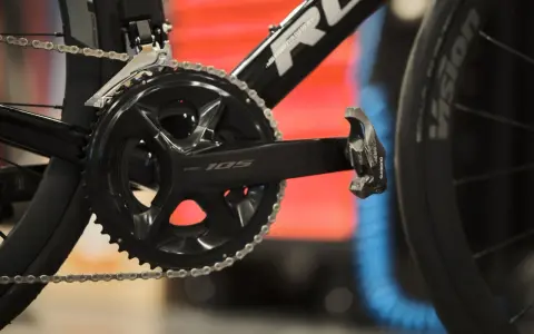 Szukasz informacji, jak dobrać korbę do roweru? Zobacz zbliżenie na czarną korbę Shimano 105 z łańcuchem i pedałem.