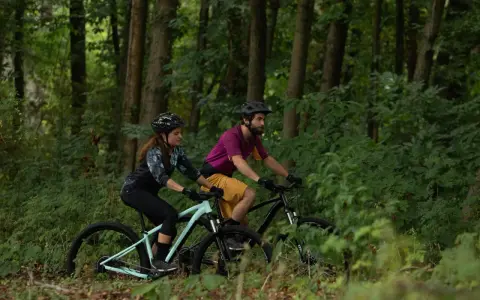 Para jadąca na rowerach górskich przez las. Czy to gravel, czy MTB? Trudno powiedzieć, ale zabawa jest przednia!